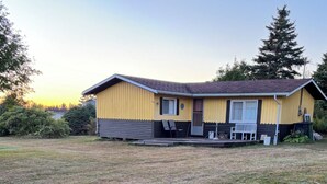 A single-story yellow house with a brown roof, a porch, and a small deck. - South shore time capsule (Canoe Cove)