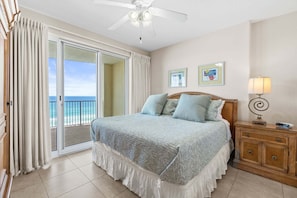 A bedroom with a bed, a nightstand, a lamp, and a view of the ocean through a sliding door. - Oceanfront Condo 7th Floor, Huge Balcony, Pools, Hot Tub, Direct Beach Access (Panama City Beach)