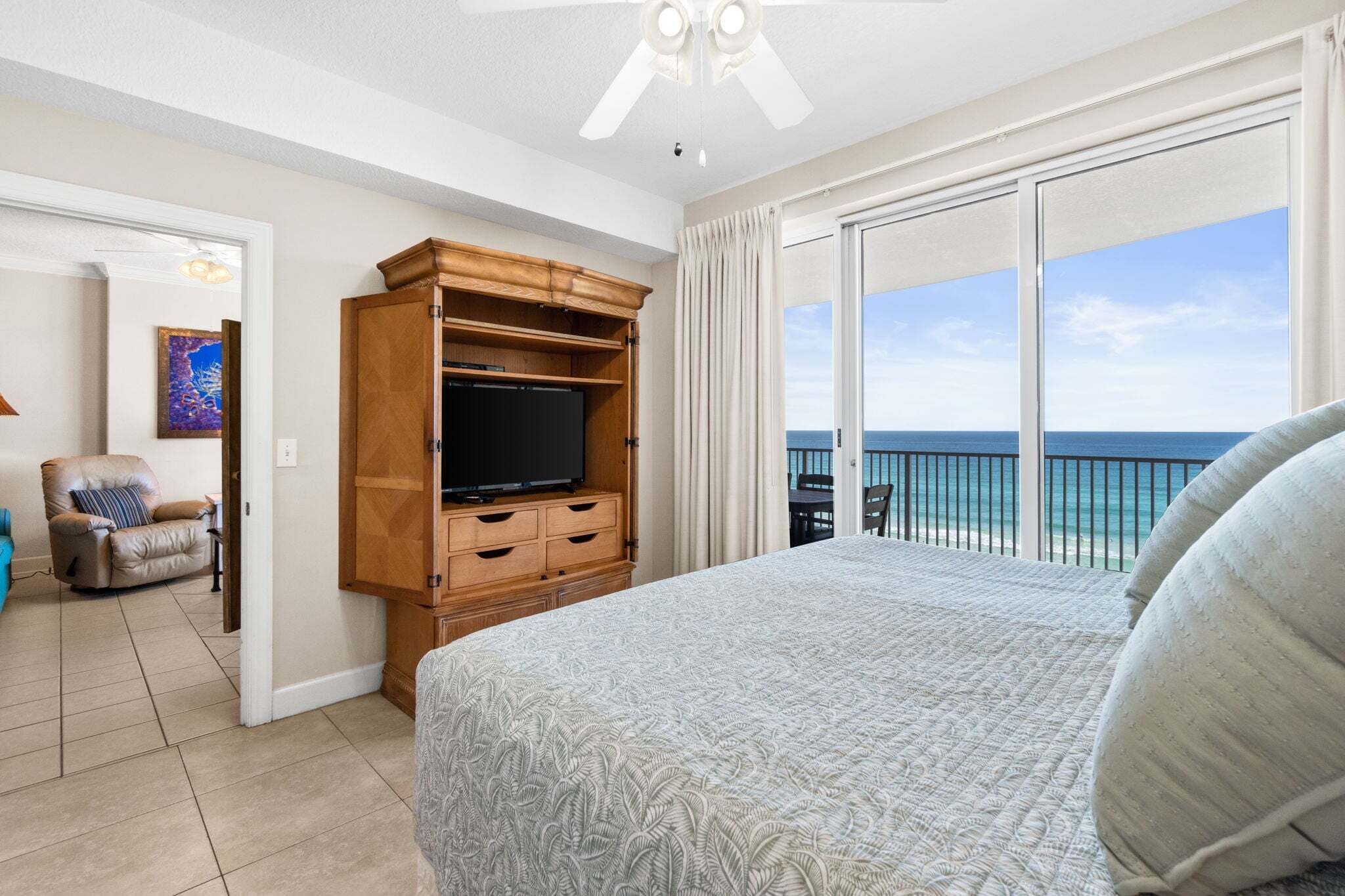 Un dormitorio con una cama grande, un mueble de entretenimiento de madera, un televisor y un balcón con vista al océano.