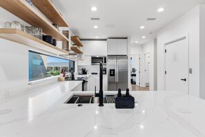 Une cuisine moderne avec des meubles blancs, un réfrigérateur en acier inoxydable, un four encastré et une fenêtre donnant sur un paysage urbain.