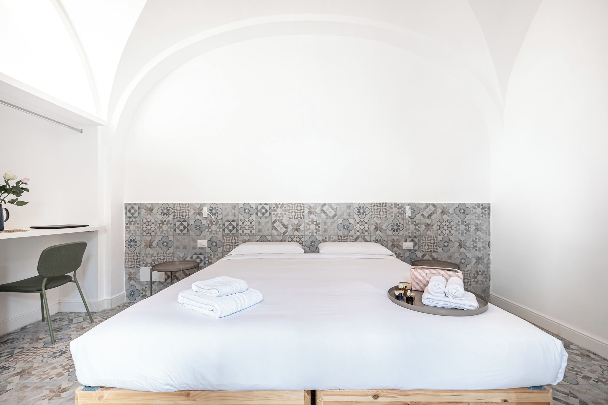 A hotel room with a large bed, a desk, and a chair. There are towels and toiletries on the bed.