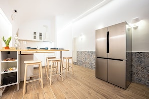 Eine moderne Küche mit Kochinsel, Barhocker, einem Edelstahlkühlschrank und einer gefliesten Spritzschutzwand.