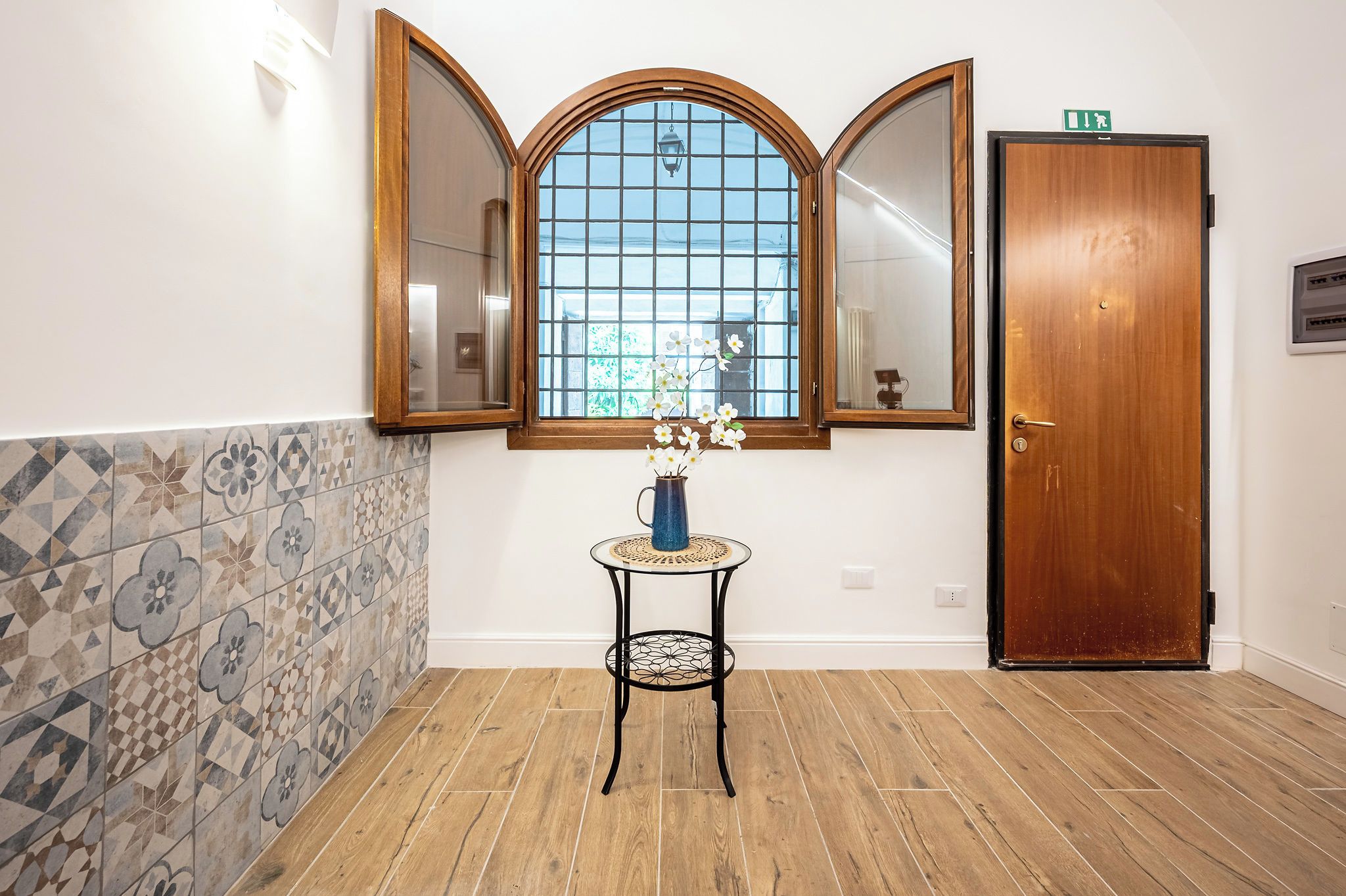 Un couloir avec un mur recouvert de carreaux, une porte en bois et une fenêtre donnant sur un paysage.