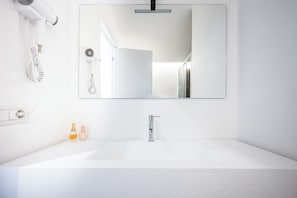 Ein modernes Badezimmer mit einem großen weißen Waschbecken, einem Spiegel und einem an der Wand befestigten Föhn.