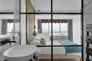 Ein modernes Hotelzimmer mit einem großen Bett, einem Badezimmer mit Waschbecken in Weiß und Meerblick.