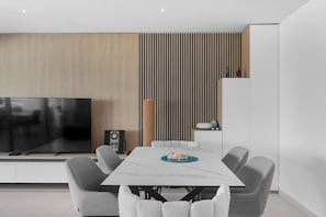 Ein modernes Wohnzimmer mit Flachbildfernseher, einer Wandverkleidung aus Holz, einem gestreiften Paneel, einem weißen Sofa und einem Esstisch mit Stühlen.