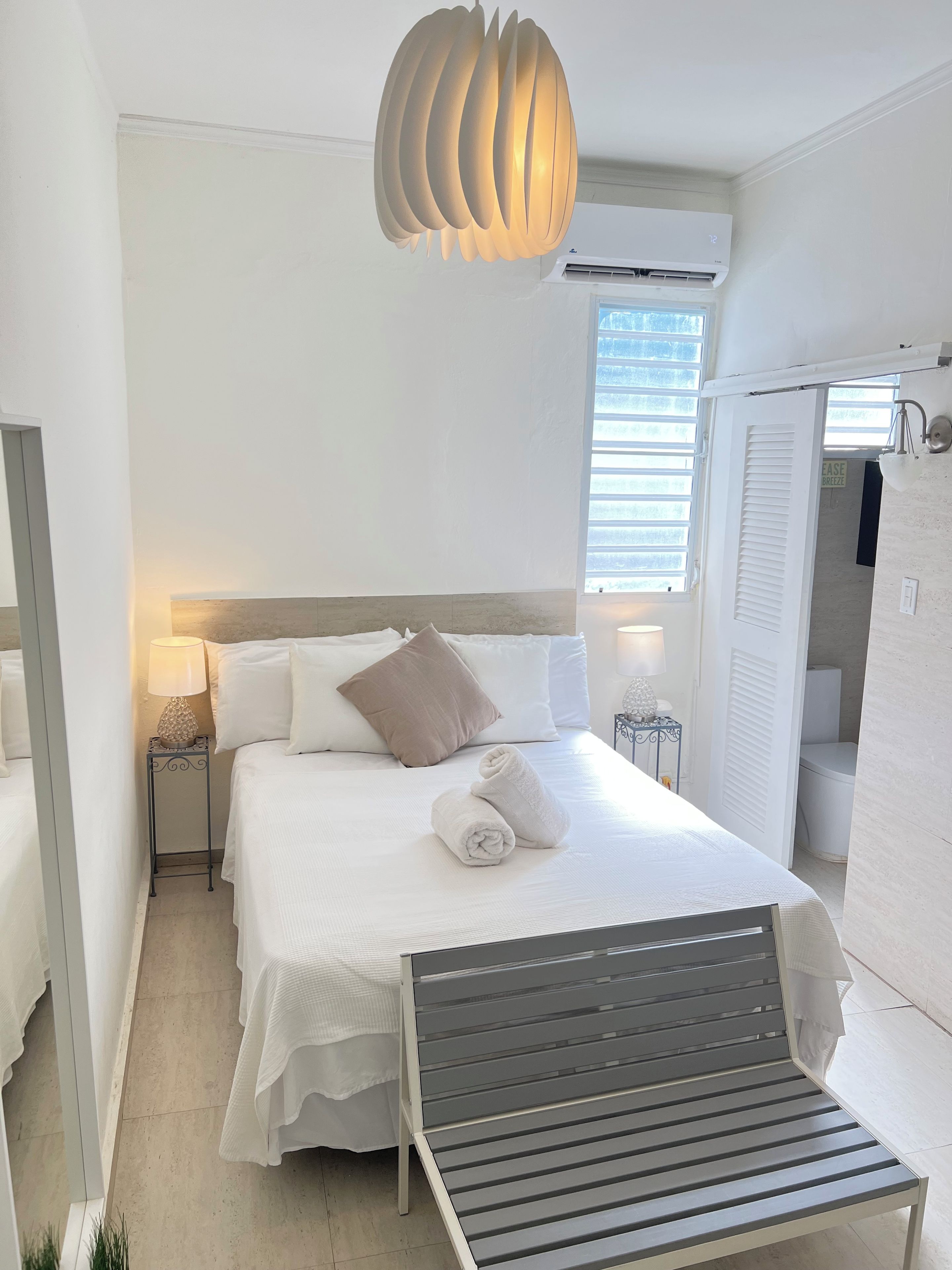 Habitación de hotel con cama, mesitas de noche, lámpara, lámpara colgante y vistas al exterior.