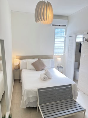A hotel room with a bed, bedside tables, a lamp, a hanging light fixture, and a view of the outside. - Beach side Ocean Park tropical studio.     High-Speed WiFi (San Juan)