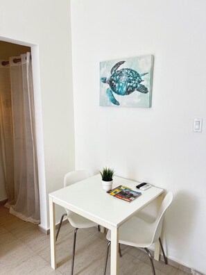 A room with a white table, two chairs, a potted plant, and a wall-mounted painting of a sea turtle. - Beach side Ocean Park tropical studio.     High-Speed WiFi (San Juan)
