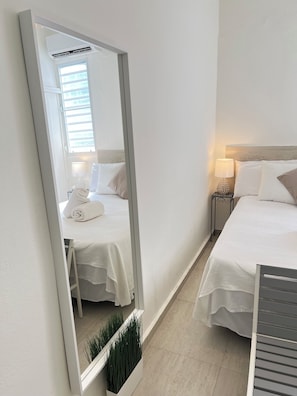 A hotel room with two beds, a large mirror, a bedside table with a lamp, and a window with blinds. - Beach side Ocean Park tropical studio.     High-Speed WiFi (San Juan)
