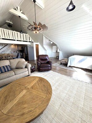 A spacious loft with a high ceiling, exposed wooden beams, a dining area, a leather chair, and a large bed. - Marvelous studio apartment with pickleball court in welcoming Orem neighborhood (Orem)