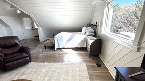 A loft bedroom with a bed, a leather chair, a wooden table, and a large window. - Marvelous studio apartment with pickleball court in welcoming Orem neighborhood (Orem)