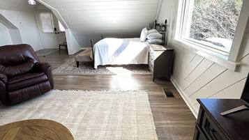 A loft bedroom with a bed, a leather chair, a wooden table, and a large window.