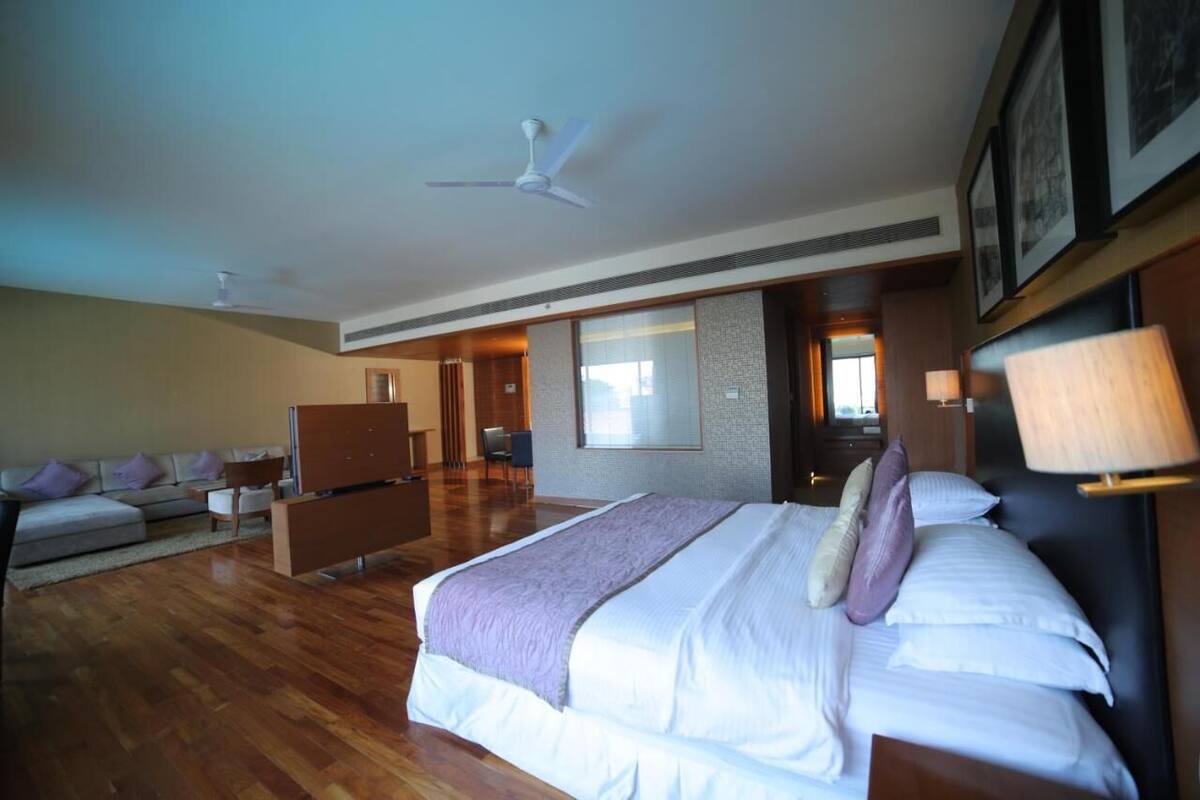A hotel room with a large bed, a sofa, a desk, and a ceiling fan.