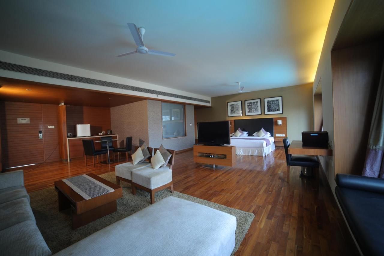 A hotel room with a living area, a bed, a TV, a desk, and a kitchenette.