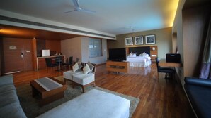 A hotel room with a living area, a bed, a TV, a desk, and a kitchenette. - Club Mahindra Kensville Golf Resort (Bavla)
