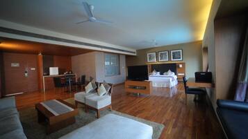 A hotel room with a living area, a bed, a TV, a desk, and a kitchenette.