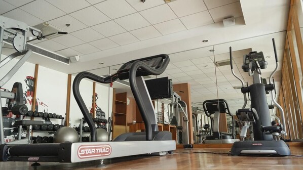 A gym with cardio equipment, weight machines, and a mirrored wall. - Club Mahindra Kensville Golf Resort (Bavla)