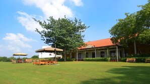 A building with a red roof, a covered outdoor seating area, and a grassy lawn. - Club Mahindra Kensville Golf Resort (Bavla)