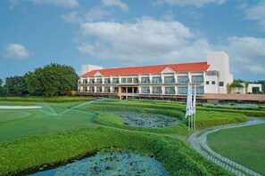 A hotel with a red roof, multiple floors, and a well-maintained garden with a pond.