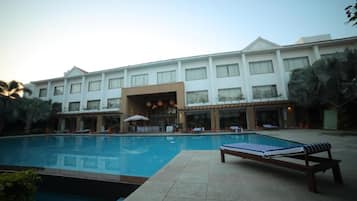 Un hotel con piscina, sillas de descanso y una zona cubierta con sombrillas.