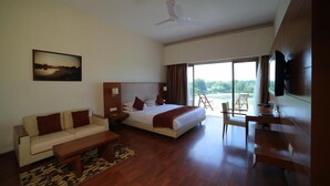 A modern hotel room with a bed, sofa, desk, and a large window offering a view of the outdoors. - Club Mahindra Kensville Golf Resort (Bavla)