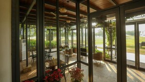A covered outdoor seating area with glass walls, wooden ceiling, and tables with chairs. - Club Mahindra Kensville Golf Resort (Bavla)