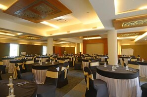 Una sala conferenze con tavoli rotondi, sedie nere con decorazioni dorate e una lavagna.