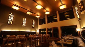 Un restaurante con paneles de techo de madera, lámparas rectangulares y un comedor con mesas y sillas.