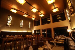 A restaurant with wooden ceiling panels, rectangular light fixtures, and a dining area with tables and chairs. - Club Mahindra Kensville Golf Resort (Bavla)
