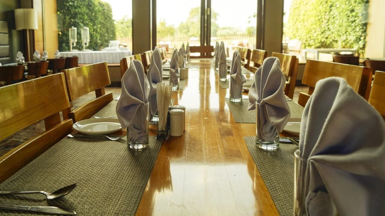 A dining area with long tables, chairs, and neatly set tables with plates, cutlery, and napkins.