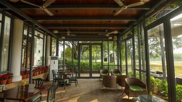 A covered outdoor seating area with tables and chairs, large windows, and ceiling fans.