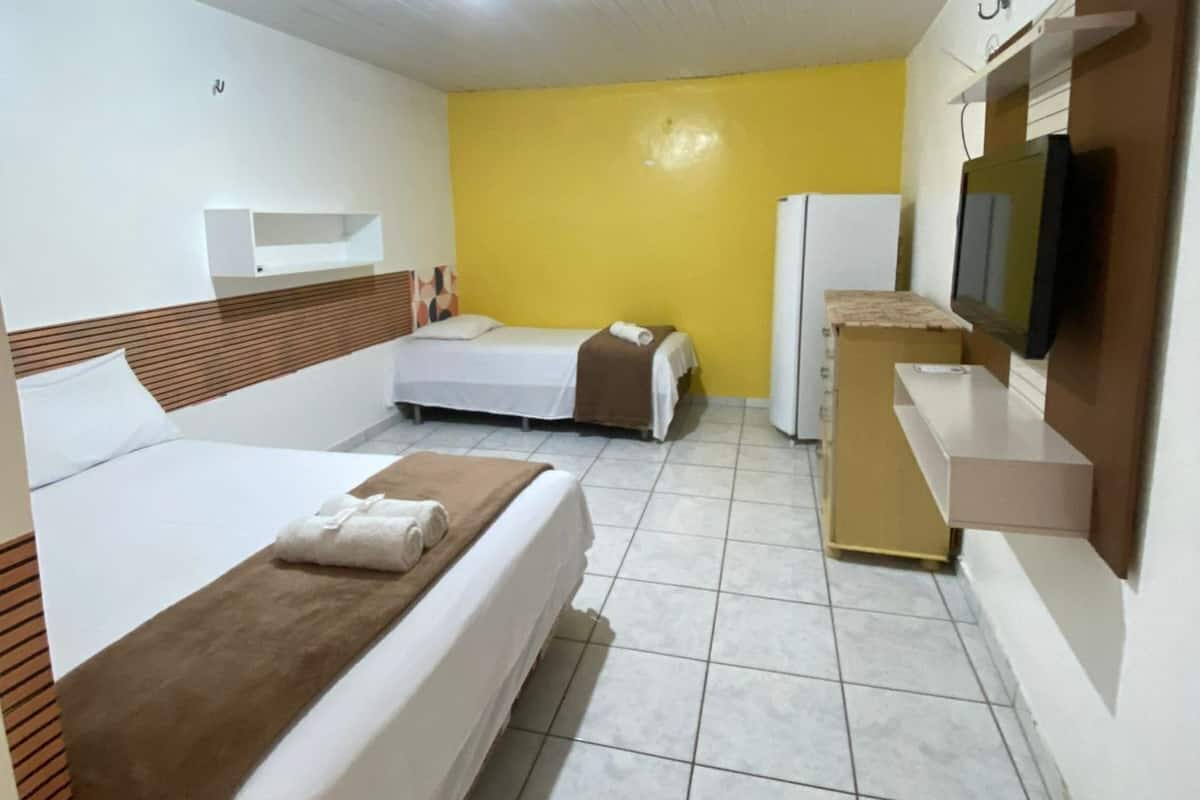 A hotel room with two beds, a small kitchenette, a television, and a yellow accent wall.