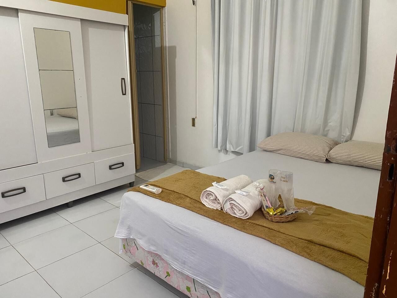 A hotel room with a bed, a wardrobe, a bathroom, and a window with curtains.
