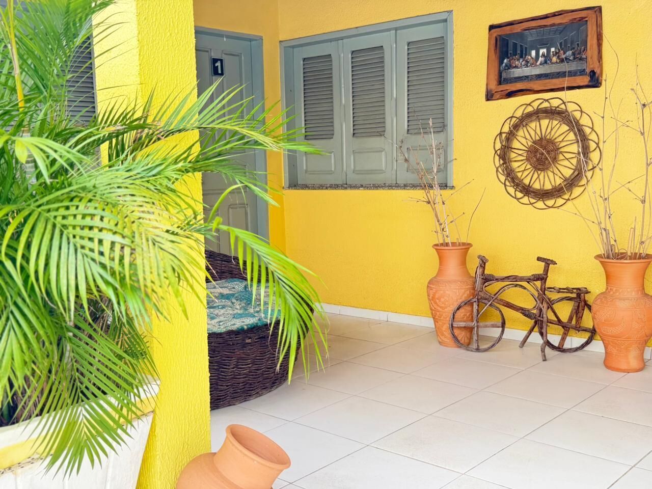 A room with a yellow wall, a wicker chair, a bicycle, and potted plants.