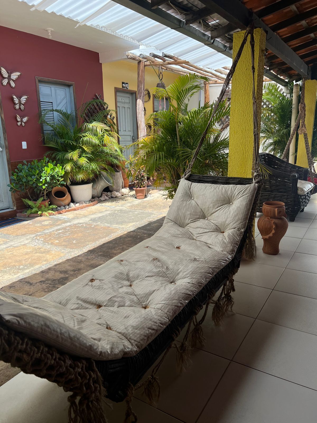 A hammock chair in a covered outdoor area with potted plants and a building in the background.