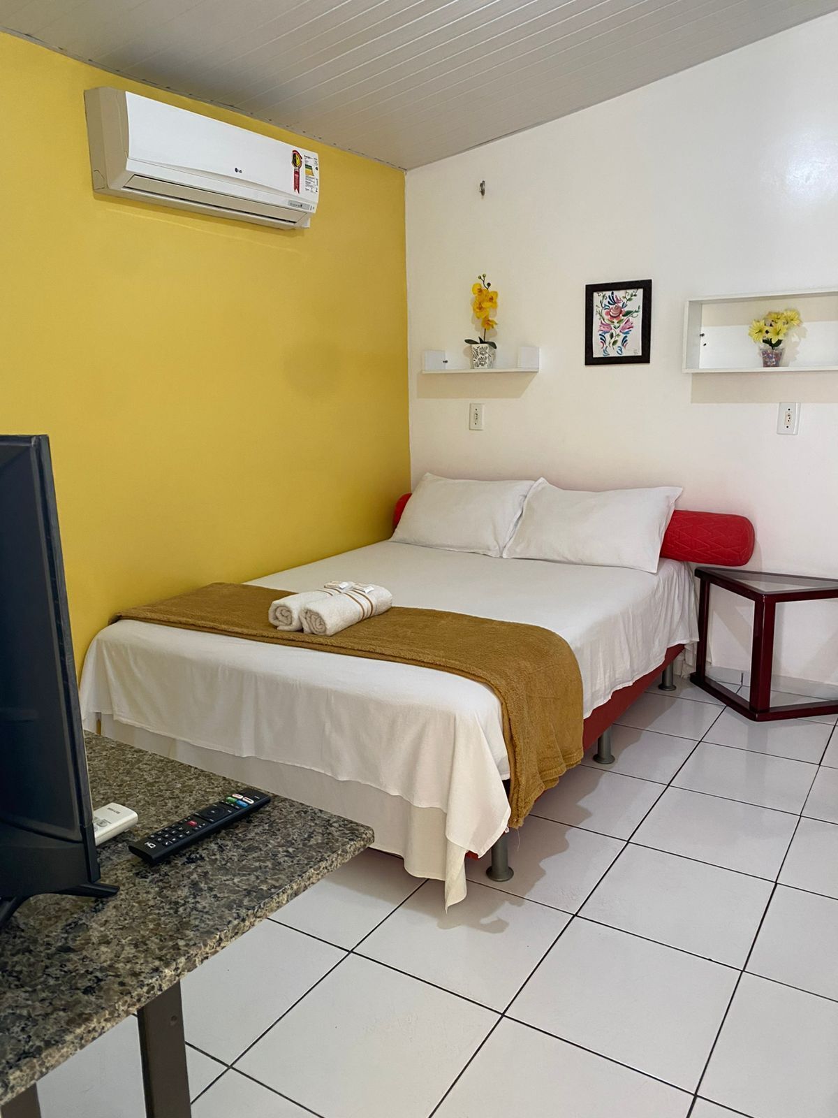 Habitación de hotel con cama, televisión, control remoto, una mesita y aire acondicionado instalado en la pared.