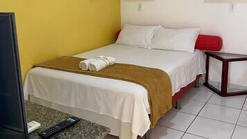Habitación de hotel con cama, televisión, control remoto, una mesita y aire acondicionado instalado en la pared.