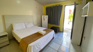 A hotel room with a bed, a refrigerator, a small table, and a window with curtains. - Bru&Mar Pousada Parnaíba (Parnaíba)