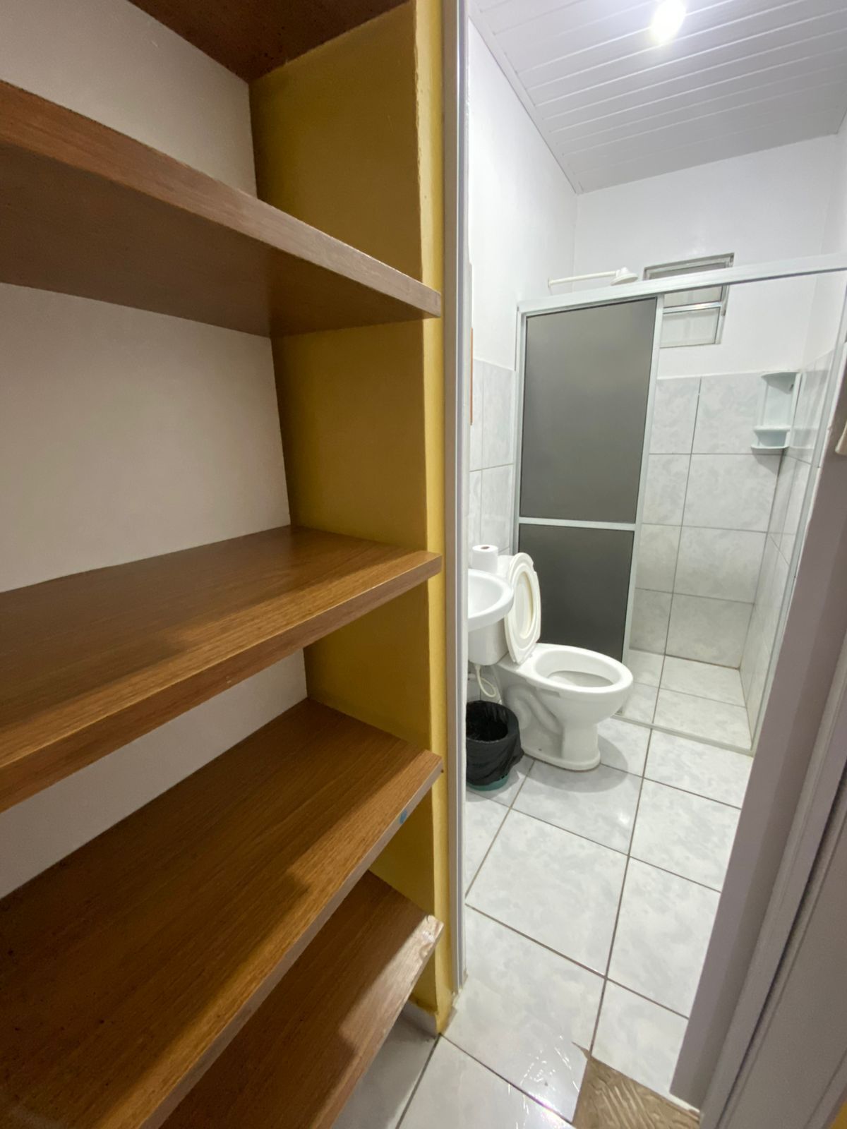 Une salle de bain avec des toilettes, un espace douche et des étagères en bois.