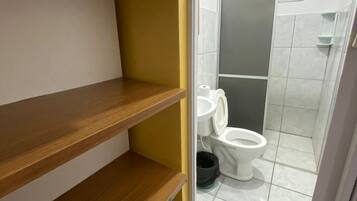 Une salle de bain avec des toilettes, un espace douche et des étagères en bois.