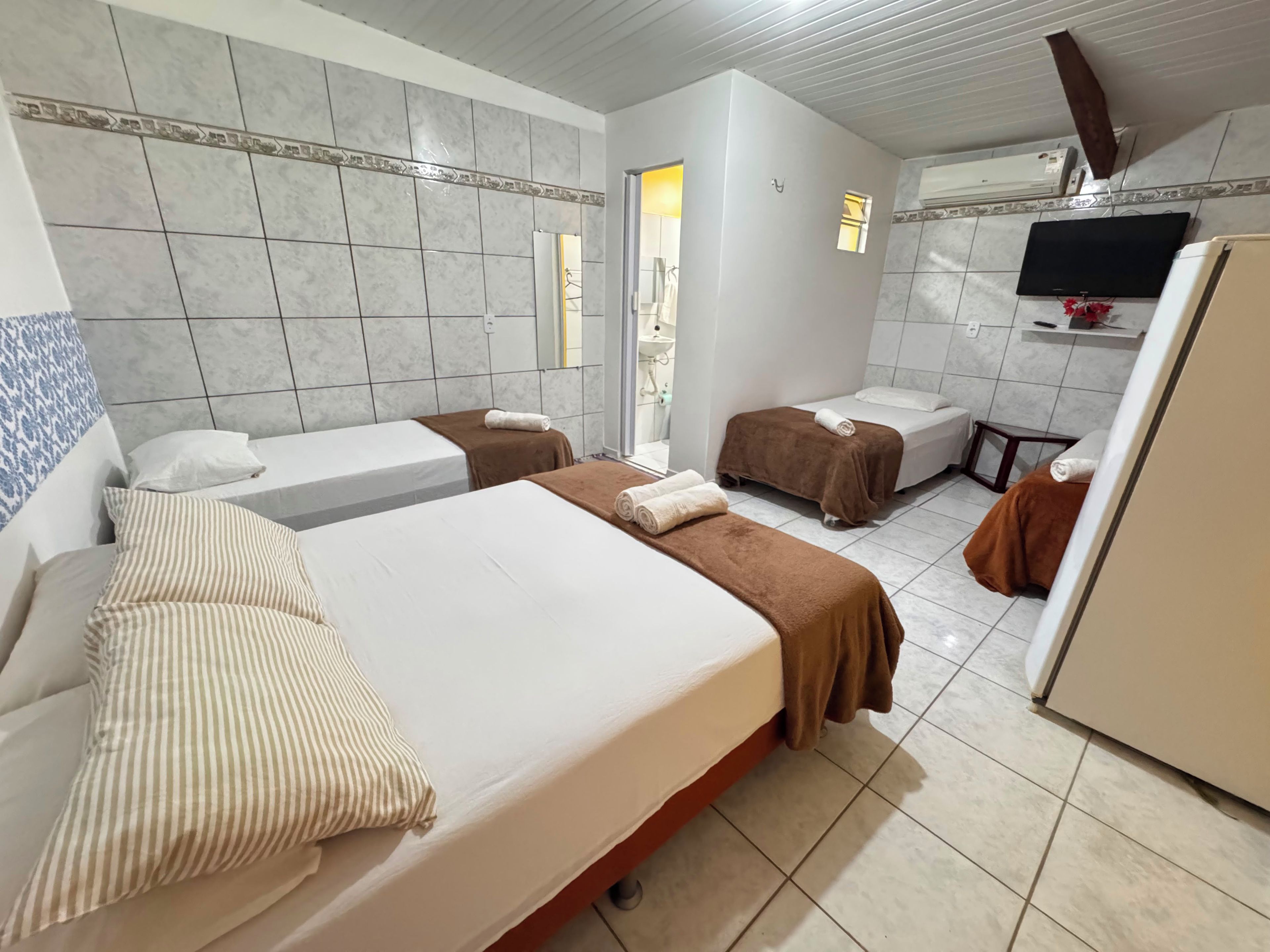 A hotel room with two beds, a small kitchenette, a television, and a bathroom with a shower.