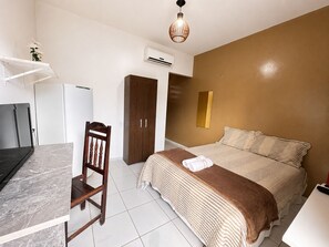 Un dormitorio con cama, una silla, un escritorio, un equipo de aire acondicionado y un espejo montado en la pared.