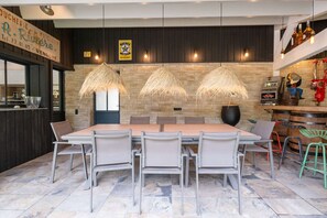 A modern dining area with a large wooden table, grey chairs, and hanging light fixtures. - Gorille - Family home with heated pool (STE MARIE DE RE)