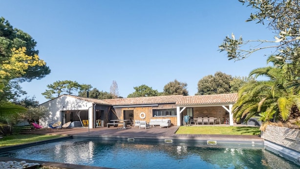 Een modern huis met een zwembad, buitenmeubilair en een overdekt terras.