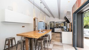 Een moderne keuken met een houten eiland, barkrukken, hanglampen en uitzicht op de omgeving.