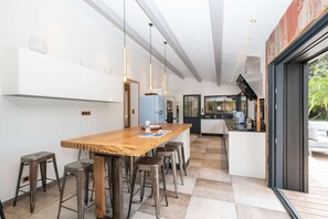 Eine moderne Küche mit einer Holzinsel, Barhocker, Pendelleuchten und Blick ins Freie.