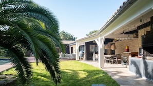 Een overdekt terras buiten, met een barbecue, zitgedeelte en een zwembad.