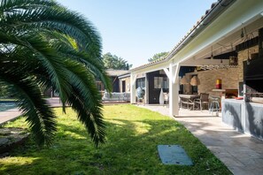 Eine überdachte Terrasse im Freien mit Grill, Sitzgelegenheit und Pool.
