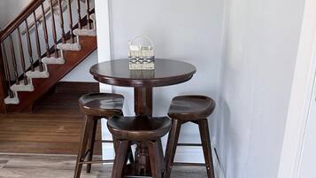 A dining area with a round table and four stools, a wicker basket on the table, and a staircase in the background.